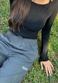 Camiseta negra de manga larga combinada con pantalones jogging ligeros grises de cintura elástica con un logo. La persona está sentada en la hierba con una postura relajada.