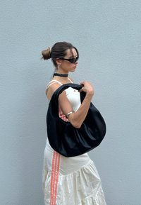 Fekete bőr hobo táska sima felülettel és széles fogantyúval. A modellen fehér ruha van piros csíkokkal és napszemüveg. Egyszerű, elegáns dizájn.