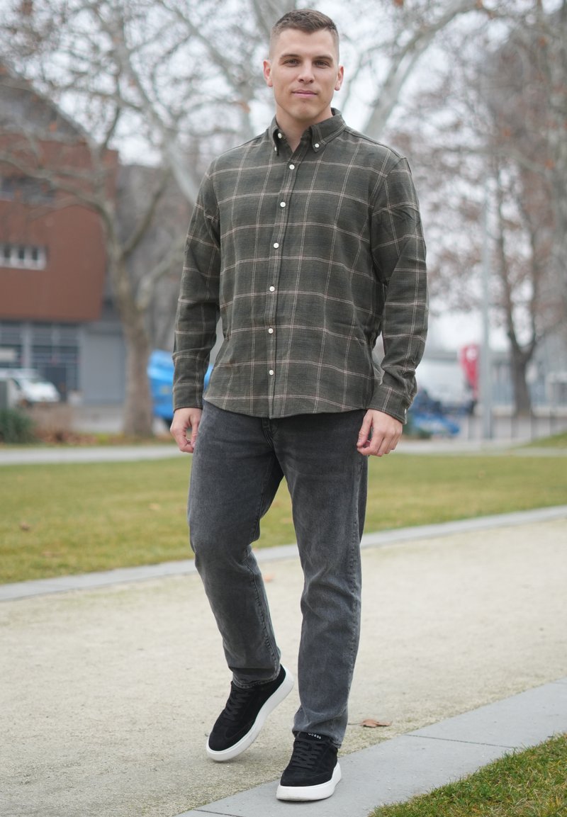 Camicia a quadri verde scuro con linee bianche e viola chiaro, abbinata a jeans grigio scuro e sneaker nere con suola bianca.