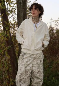 Lys beige glidelåsjakke med strukturert finish, kombinert med løstsittende cargobukser med et subtilt, marmorert mønster i jordfarger.