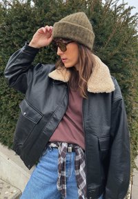 Crna kožna jakna s kremastim krznom na ovratniku, smeđa majica, izblijedjele plave traperice i zelena pletena kapa, upotpunjeni sunčanim naočalama.