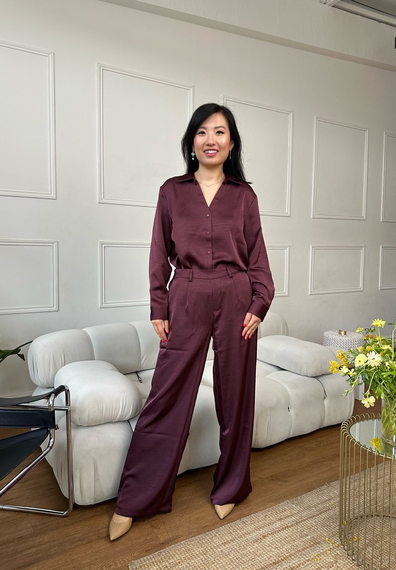 Ensemble chemise en satin marron et pantalon à jambes larges. Comprend un col, une fermeture à boutons sur le devant et une coupe ajustée. Porté avec des talons beiges pointus et des bijoux minimalistes.