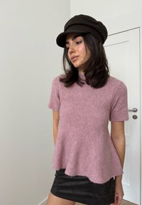 Pull à manches courtes rose clair avec un ourlet évasé, en tissu texturé. Associé à une mini-jupe noire et une casquette foncée.