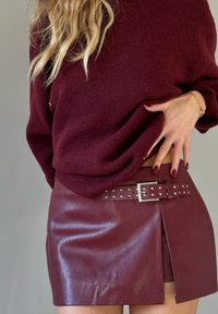 Bordeaux læder mini nederdel med en sideslidser, udstyret med et nittet bælte og en glat tekstur. Sæt sammen med en matchende strikket sweater.