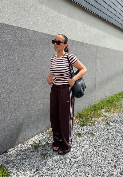 Camiseta ajustada a rayas en rosa claro y blanco, combinada con pantalones deportivos holgados marrones con franjas laterales blancas. Bolso negro y gafas de sol.
