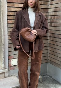 Blazer de pana marrón sobre un jersey de cuello alto blanco, combinado con pantalones de pana marrón a juego. Sosteniendo un bolso pouch marrón texturizado.