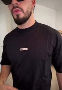 Fekete pamut rövid ujjú póló, elöl kis téglalap alakú fehér címkével, amelyen piros betűkkel az "MARNI" felirat található.