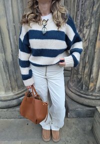 Navy und creme gestreifter Strickpullover, weiße Hose mit Reißverschluss vorne, braune Handtasche und braune Schuhe. Der Pullover hat einen Oversize-Schnitt und eine strukturierte Oberfläche.