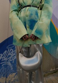 Χαλαρή μπλέιζερ με πράσινο-μπλε σχέδιο, ασημί μεταλλικά παντελόνια και μια καμπυλωτή ασημί τσάντα με χερούλι, που διαθέτει ανάγλυφη επωνυμία στην κάτω πλευρά.