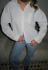 Weißes Button-up-Hemd aus Baumwolle, mit Tasche, langen Ärmeln und lockerer Passform, kombiniert mit blauen Schlagjeans.