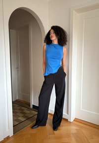 Top bleu sans manches avec un détail froncé sur le côté, associé à un pantalon noir taille haute à jambes larges. Textures de tissu lisses ; design minimaliste.