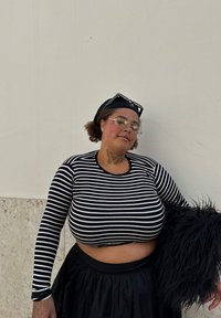 Haut à rayures noires et blanches à manches longues, jupe noire et accessoire noir duveteux. Des lunettes claires et une casquette noire complètent la tenue.