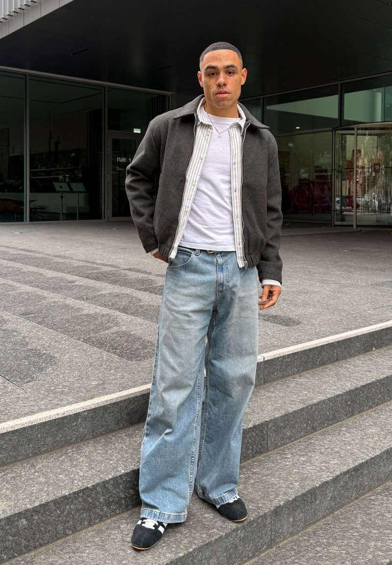Gray wool blend jacket over a white shirt with a striped button-up, light blue wide-leg denim jeans, and black shoes with white straps.