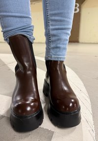 Brune skinn ankelstøvler med en blank finish, tykke svarte gummisåler, elastiske sidepaneler og runde tær, kombinert med lyseblå jeans.