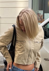 Jachetă scurtă de culoare bej deschis, cu mâneci lungi, două buzunare frontale cu fermoar și închidere cu fermoar dreaptă. Purtați cu blugi cu talie înaltă.