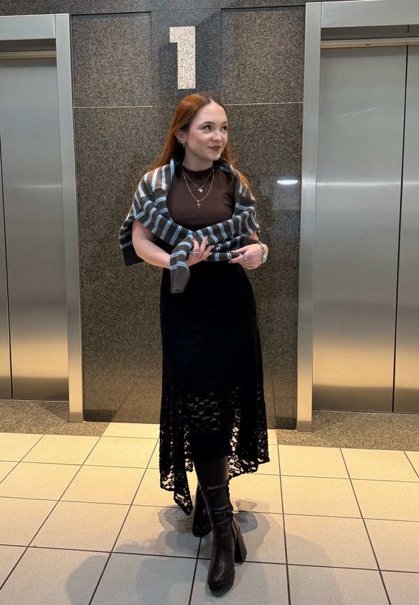 Young woman in black dress and boots stands between two lifts under a large number "1" on a stone wall.