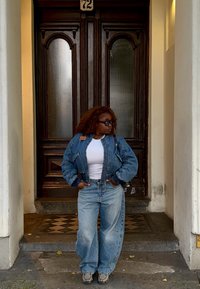 Denimjakke med en litt kortere passform og ribbestrikkede mansjetter, kombinert med løstsittende lyseblå jeans. Hvit topp og mørke solbriller.