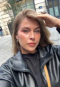 Musta keinonahkainen takki vetoketjullisella kauluksella, päällä musta paita. Henkilöllä on vaaleanruskeat hiukset ja siniset silmät.