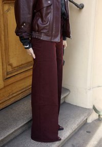 Burgundy wide-leg pants made from cotton, paired with a brown leather jacket featuring silver hardware, set against a staircase background.
