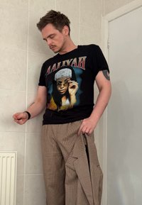 Maglietta nera con grafica di una donna con occhiali da sole, abbinata a pantaloni a quadri beige. Il tessuto sembra leggero con una finitura strutturata.