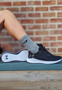 Baskets de sport noires avec un dessus en maille et une semelle blanche, dotées d'une semelle texturée et de lacets noirs. Chaussettes grises côtelées avec un logo noir.