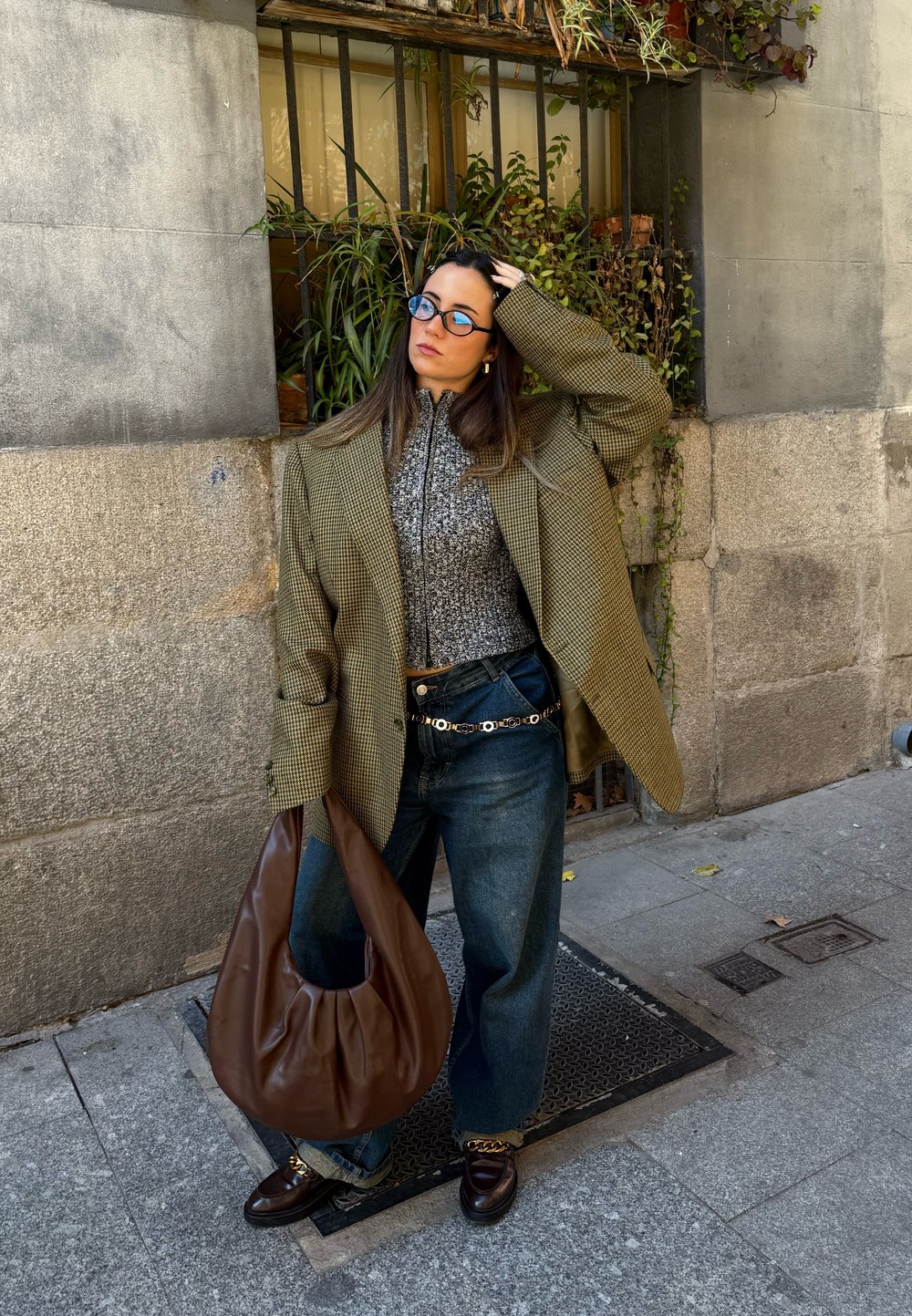 Prevelik zeleni houndstooth blejzer, sivi pulover z visokim ovratnikom, modre očala, ohlapne modre kavbojke, rjava usnjena hobo torba in loafers s podrobnostjo verige.