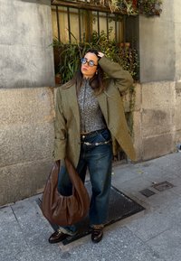 Prevelik zeleni houndstooth blejzer, sivi pulover z visokim ovratnikom, modre očala, ohlapne modre kavbojke, rjava usnjena hobo torba in loafers s podrobnostjo verige.
