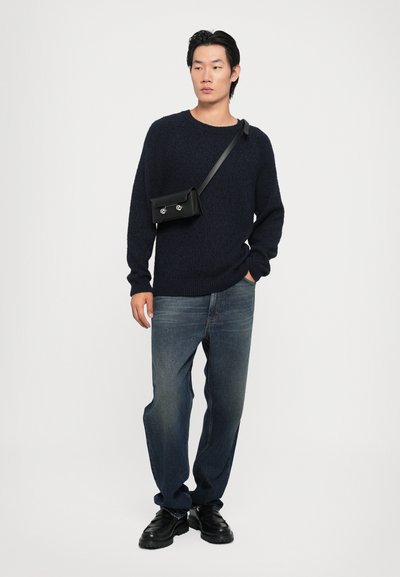 Suéter texturizado azul marino, jeans de mezclilla oscuros, bolso cruzado negro con herrajes plateados y zapatos negros gruesos. Un atuendo sencillo y casual.