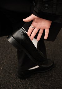 Mustast nahast libisev king, millel on sile tekstuur, ümmargune varvas ja madal konts, kantud valge sukaga ja mustade pükstega.