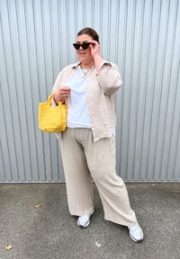 Šviesiai smėlinis lininis marškinis, baltas marškinėlis ir laisvi smėliniai kelnių. Laiko geltoną pintą rankinę, mūvi juodus katės akių akinius ir sportinius batus.