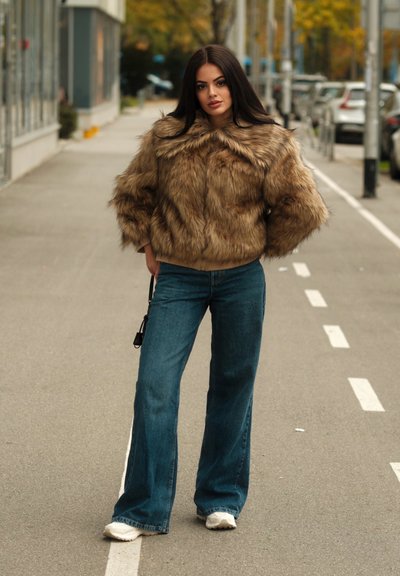 Chaqueta de pelo sintético en color beige, diseño corto con mangas anchas y cuello redondo, combinada con jeans de campana azules y zapatillas blancas.