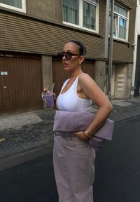 Žena u bijelom topu i svijetloplavim hlačama drži usklađenu torbicu i ljubičasti napitak sa slamkom na kamenoj ulici.