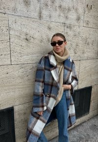 Plavi i bijeli karirani vuneni kaput s klasičnim ovratnikom, uparen s bež rebrastim dolčevitkom i plavim trapericama.