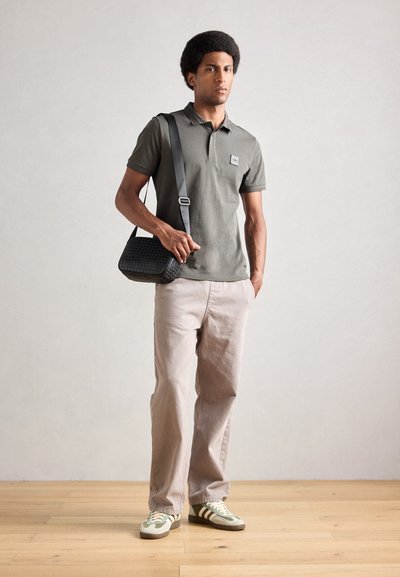 Camisa polo verde oliva de manga corta, pantalones de pierna ancha beige y bolso bandolera negro texturizado. Zapatillas de deporte a rayas blancas y verdes.