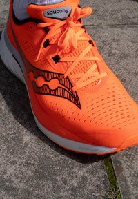 Erkki jooksujalats heledas oranžis värvitoonis, millel on hingav sisedoos, tekstuuriga muster, mustad aktsendid ja valge PWRRUN tald, millel on lamedad paelad.