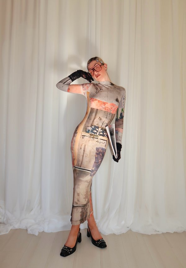 Femme posant dans une longue robe à motifs avec des gants noirs, des lunettes surdimensionnées, des barrettes dans les cheveux et des talons noirs, tenant un magazine roulé.