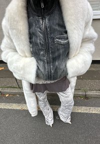 Bílý kabát z umělé kožešiny přes tmavě modrou džínovou bundu se zipem a kapsami, v kombinaci se šedými kalhotami s texturovaným vzorem a špičatými podpatky.