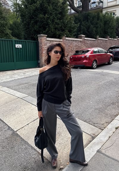 Suéter negro con los hombros al descubierto combinado con pantalones de pierna ancha gris a rayas. Los accesorios incluyen un bolso negro y gafas de sol delgadas. Zapatos marrones.