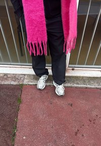 Μαύρο παντελόνι, φωτεινός ροζ μάλλινος κασκόλ με φούντες και ασημί αθλητικά παπούτσια με �μαύρες λεπτομέρειες σε υφή επιφάνειας.