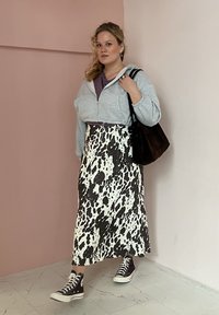 Γκρίζα φούτερ με φερμουάρ, μοβ μπλούζα, μεσαίου μήκους φούστα με σχέδιο αγελάδας σε άσπρο και μαύρο, καφέ τσάντα και μαύρα αθλητικά παπούτσια με λευκή σόλα, πάνω σε μάρμαρο.