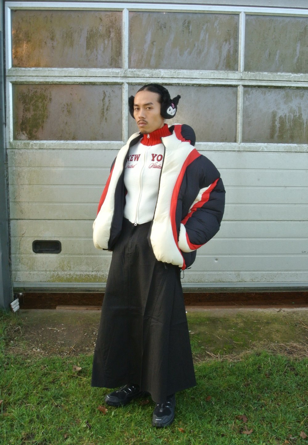 Jachetă pufoasă alb-negru cu accente roșii, pulover alb mulat cu textul "NEW YORK", fustă lungă neagră și pantofi negri, purtată în aer liber.
