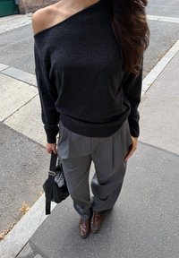 Maglione nero off-shoulder, pantaloni larghi a righe grigie, scarpe marroni e borsa nera. Morbida texture in maglia con vestibilità comoda.