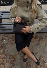 Beige trenssitakki, jossa on napit, musta käsilaukku, mustat lyhyet housut ja mustat ballerinat. Taustalla on pudonneita lehtiä ja penkki.