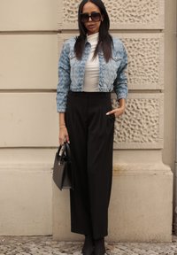 Farmerdzseki mintás ujjal, testhezálló fehér garbó, magas derekú fekete nadrág és fekete táska. A sötét napszemüveg teszi teljessé a külalakot.