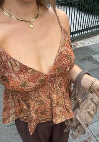 Peplum topp i oransje og brunt blomstertrykk, med dyp V-hals, samlet midje og lett materiale. Tilbehør: beige veske.