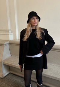 Černé oversized sako, černý svetr, bílá spodní košile a černá minisukně. Vlnený klobouk bucket. Černé punčocháče a kotníkové boty. Hladké textury.