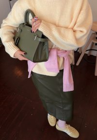 Olivengrønn skinnhåndveske, teksturert kremfarget genser, rosa genser knyttet rundt livet, tettsittende olivengrønn skjørt, gule joggesko, lyse lilla sokker.