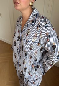 Blå og hvit stripet pysjamassett med illustrasjoner av tegneseriehunder. Har krage, lomme og blå piping langs kantene.