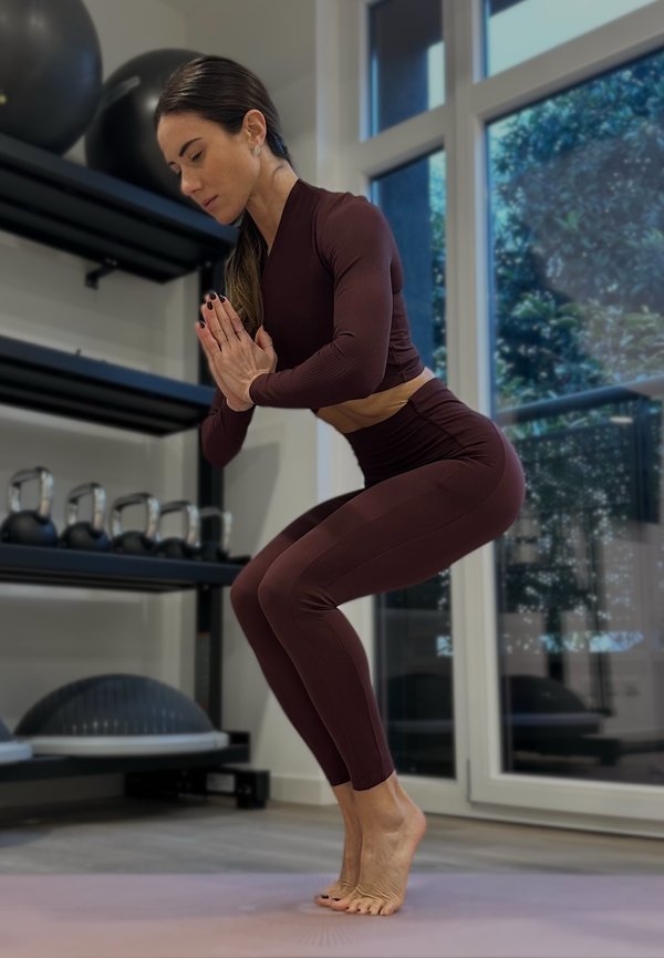 Vrouw in sportkleding balanceert op haar tenen in een yogahouding op een matje in een sportschool met kettlebells en fitnessapparatuur.