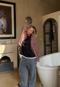 Grå, store bukser, sort-hvide lagdelte skjorter og en ternet rød skjorte. Baggrunden viser et hvidt badekar og stenmure.